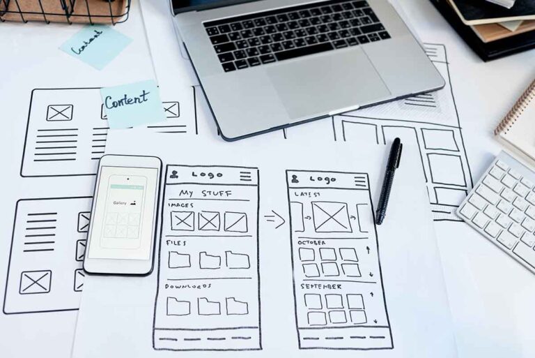 Website wireframe sketches and mobile mockups on desk with laptop and keyboard