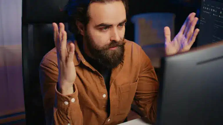 Frustrated bearded man raising hands at computer screen