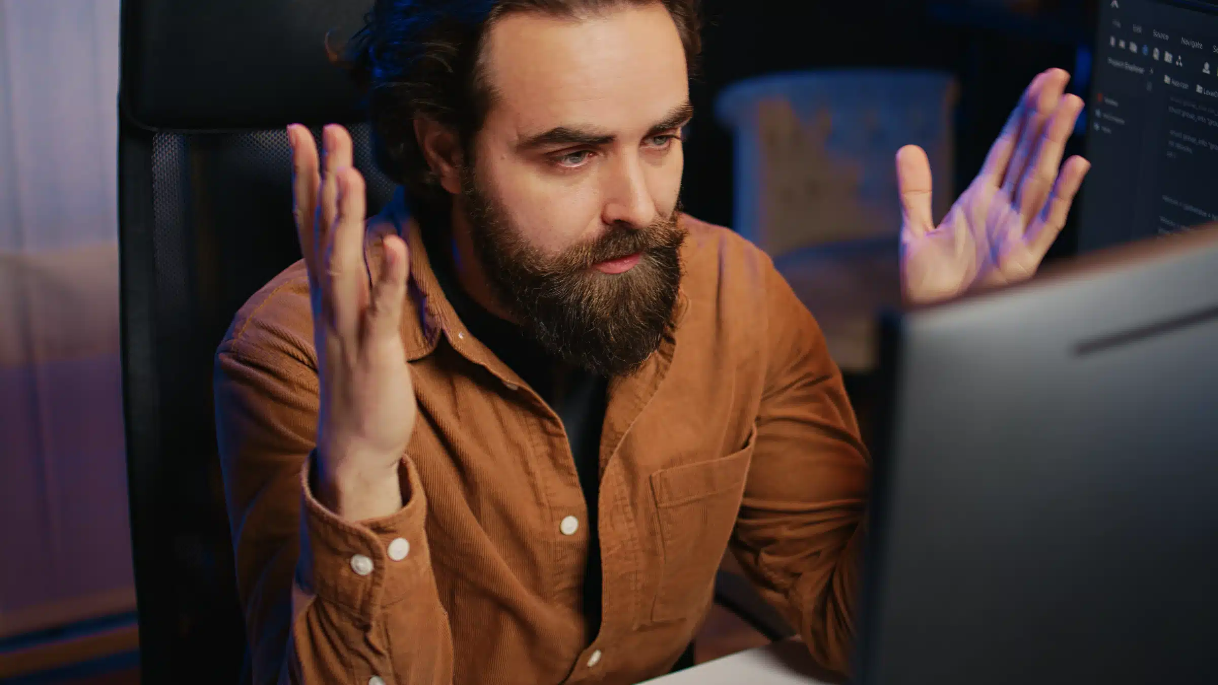 Frustrated bearded man raising hands at computer screen