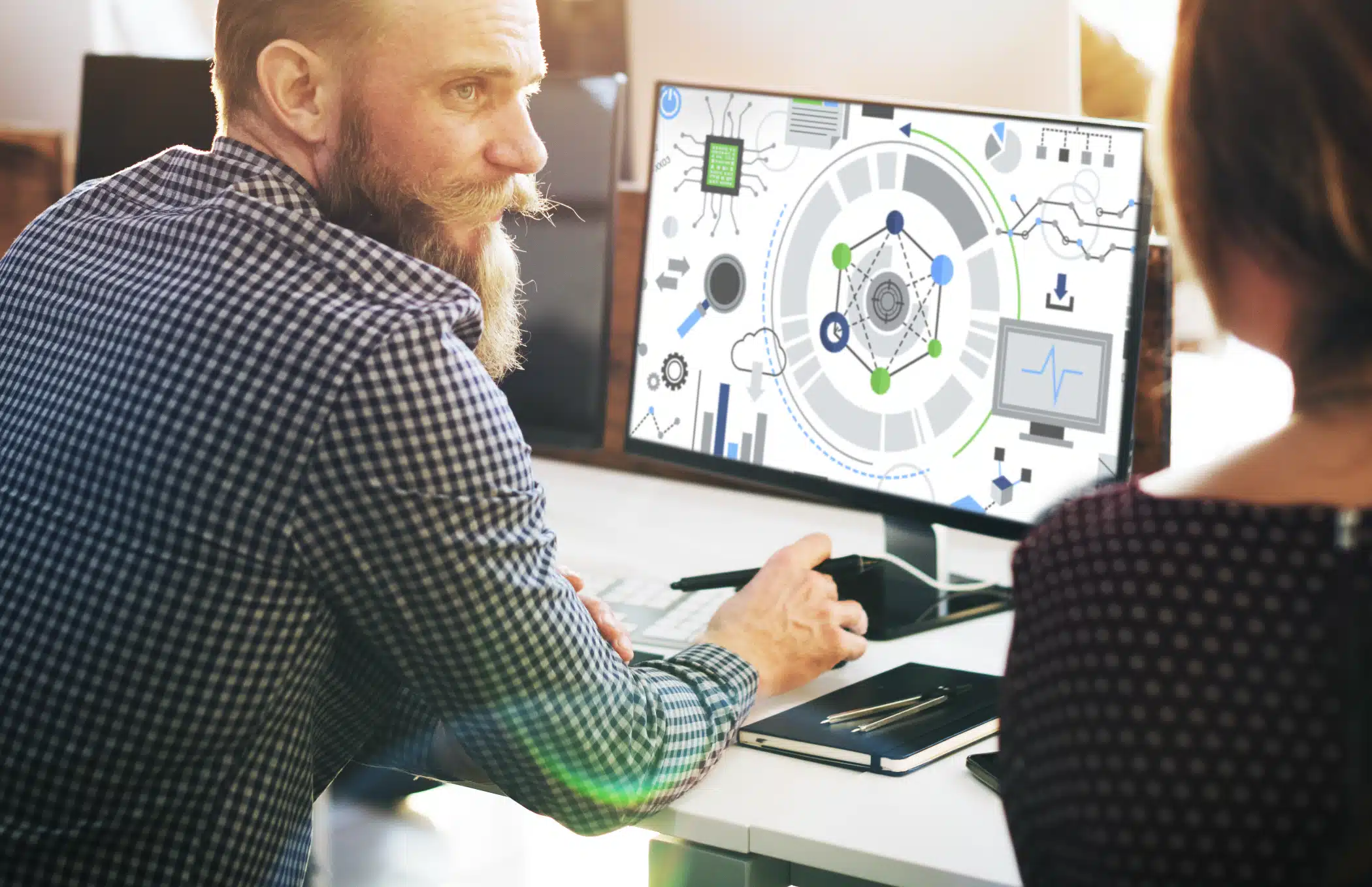 Two professionals reviewing technology dashboard on computer monitor