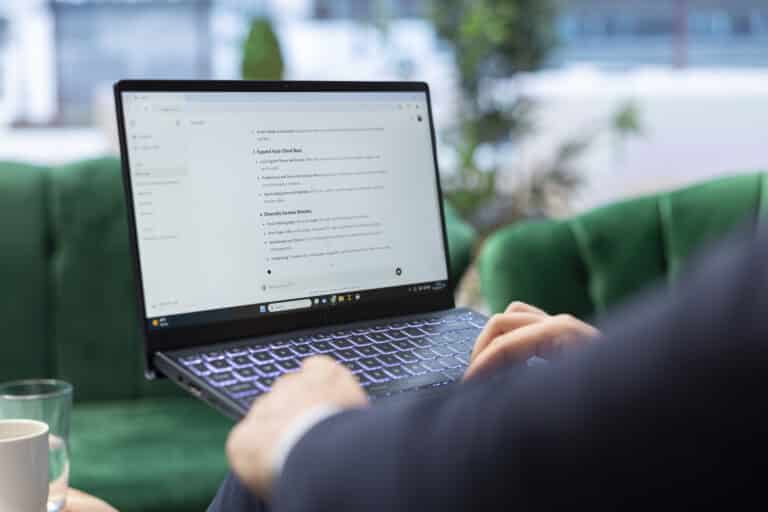 Over-the-shoulder view of a person typing on a laptop showing an AI chat tool being used to ask about growing a photography business.