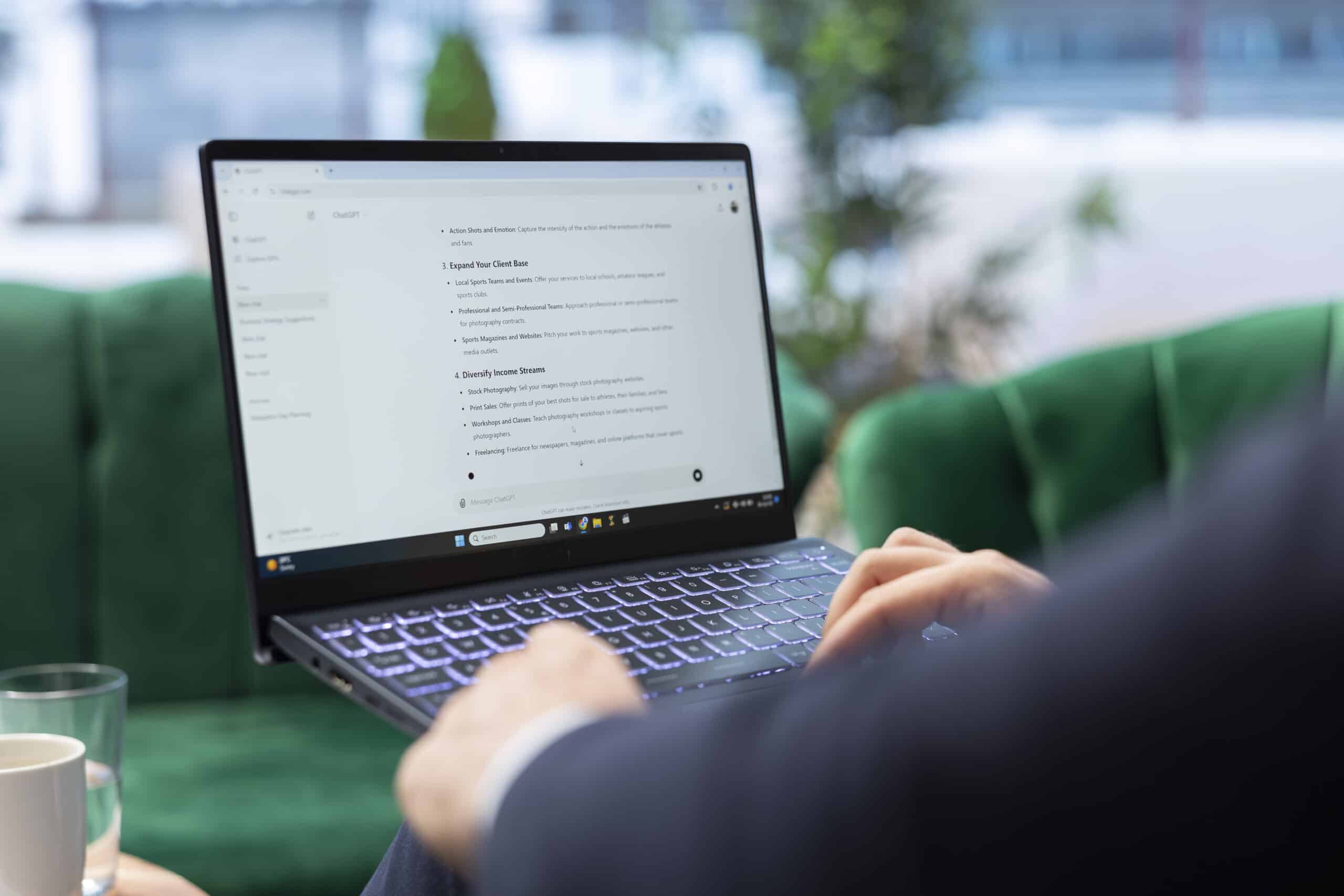 Over-the-shoulder view of a person typing on a laptop showing an AI chat tool being used to ask about growing a photography business.
