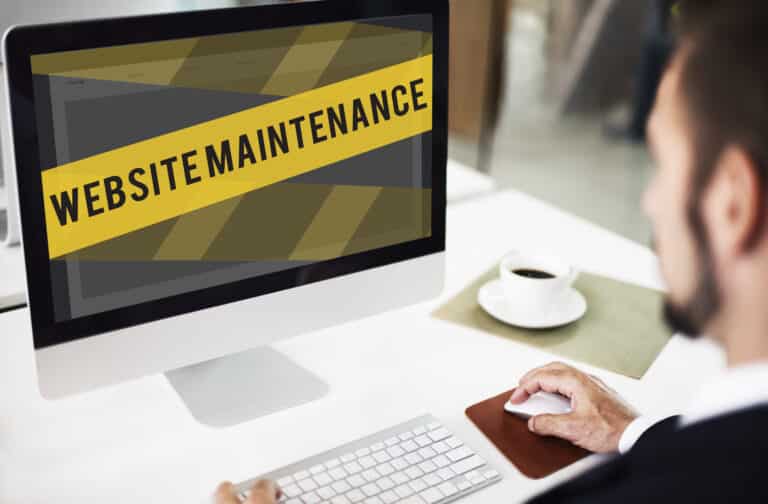 A man at a desktop computer looking at a site covered by a yellow Website Maintenance banner.
