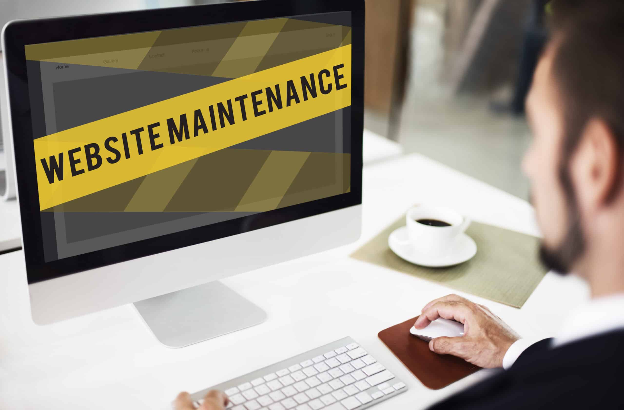 A man at a desktop computer looking at a site covered by a yellow Website Maintenance banner.